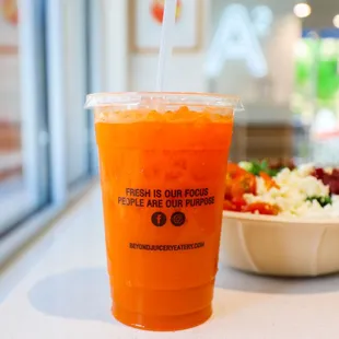 a plastic cup of orange juice with a straw