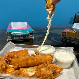 a hand dipping a piece of chicken wings