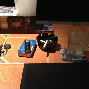 a glass of water, a cigarette, keys, and other items on a tile floor