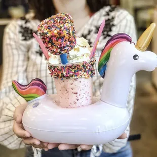 The Unicorn Shake -- strawberry shake, vanilla icing rainbow sprinkle rim, unicorn bark, sugar stars, marshmallows, whip, inflatable unicorn