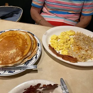 Two regular pancakes, scrambled eggs, hash browns, bacon. One half of bacon removed.