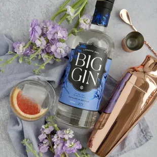 a bottle of big gin gin next to a cocktail shaker and purple flowers