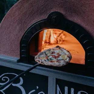 a pizza being taken out of a brick oven