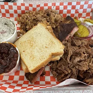 3 Meat Platter with chopped brisket, pulled pork, a rib, white potato salad, toast, baked beans, pickles, and onions.