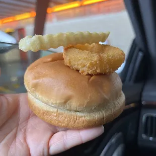 a hand holding a sandwich with fried fish on it