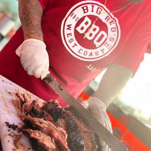 a man in a red shirt and white gloves cutting meat
