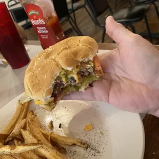 a hand holding a half eaten hamburger and fries