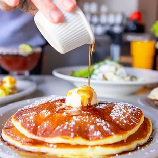 a person pouring syrup onto a stack of pancakes