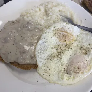 Country fried steak with gravy eggs and grits.