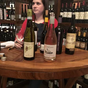 a woman sitting at a table with bottles of wine