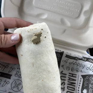 a hand holding a burrito in a styrofoam container
