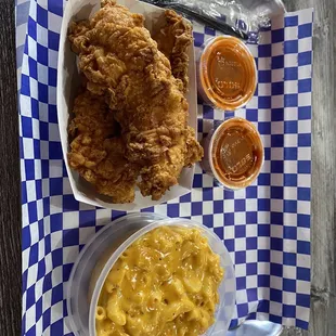 Chicken tenders with a side Mac and Cheese and buffalo sauce.