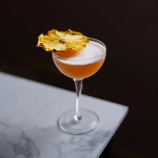 a cocktail in a coupe glass with a pineapple garnish