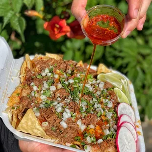 a person pouring sauce onto a plate of nachos