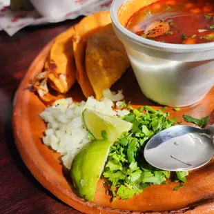 Two Birria tacos with consomme and avocado slices.