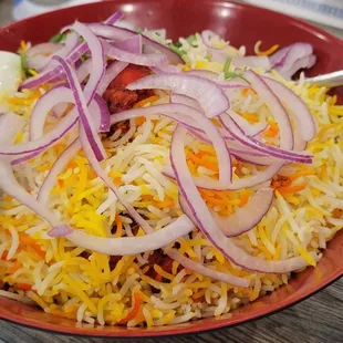 a bowl of biryani rice with onions and lime wedges