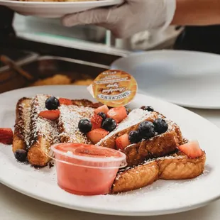 a plate of french toast with berries and powdered sugar