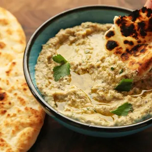 a hand dipping a piece of bread into a bowl of hummus