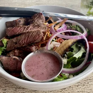 a bowl of salad with steak and onions