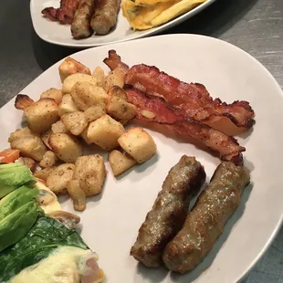Two Omelette bar plates. Omelette topped with fresh avocado with a side of sausage, bacon, and potatoes.