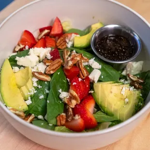 a bowl of salad with strawberries, avocado, and pecans
