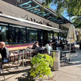 people sitting at tables outside a cafe