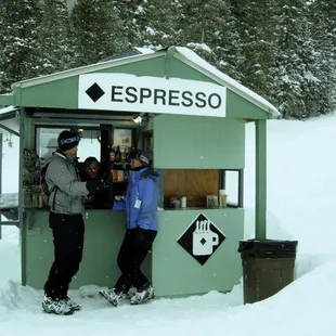 two people standing in front of a green espresso kiosk