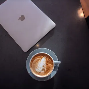 a cup of cappuccino next to an apple laptop