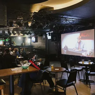 a man sitting at a table in front of a projector screen