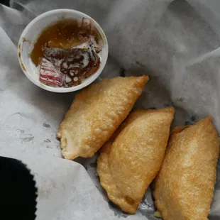 three pastries in a basket with dipping sauce