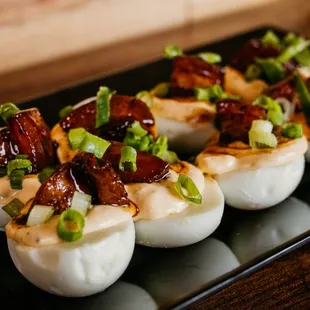 a plate of deviled eggs with bacon and scallions