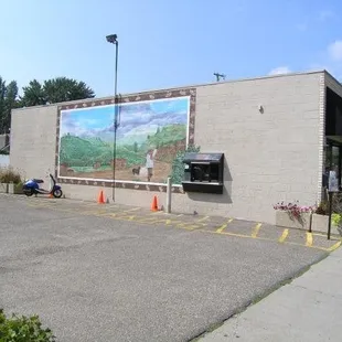 The view from the east, showing a large mural and the drive up window at Black Sheep Coffee Cafe.