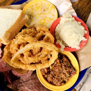 a plate of pulled pork, corn, potatoes, and onion rings