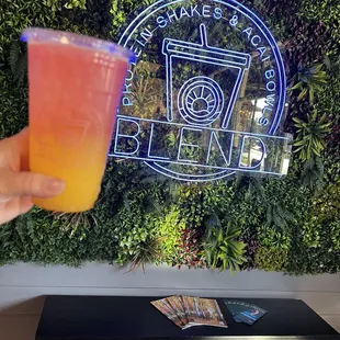 a person holding a drink in front of a green wall
