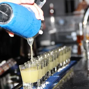 a bartender pouring a drink into shot glasses