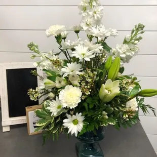 Traditional floral designed arrangement.  All whites in green glass pedestal vase.