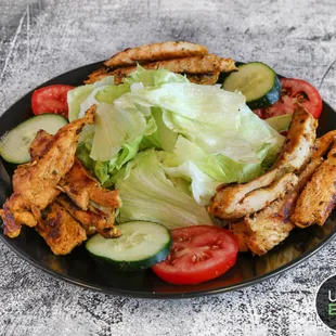 a plate of chicken, lettuce, tomatoes and cucumbers