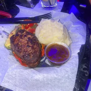 filet mignon and garlic mashed on a plastic plate on top of parchment paper that ripped when she cut the steak