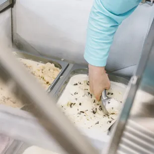 a person scooping ice cream into a container