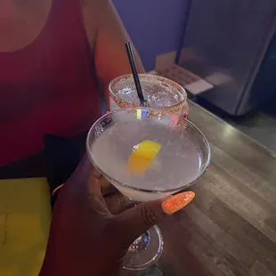 a woman holding two cocktails