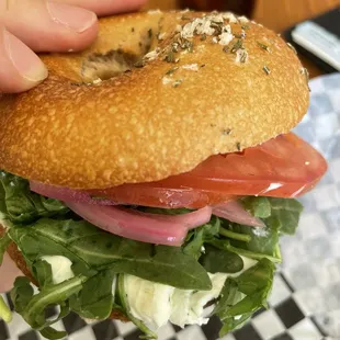 Veggie Sandwich on sea salt/rosemary bagel. Chive cream cheese spread. Pickled onions, arugula, Tomato.