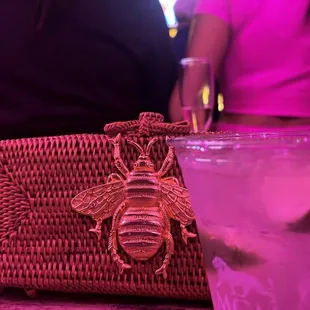 a woman sitting at a table with a straw bag and a glass of lemonade