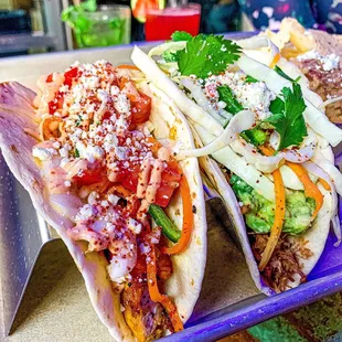 three tacos with toppings on a tray