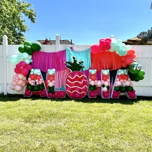 Letter marquees filled with balloons, custom pineapple filled with balloons, fringe backdrop, balloon garland
