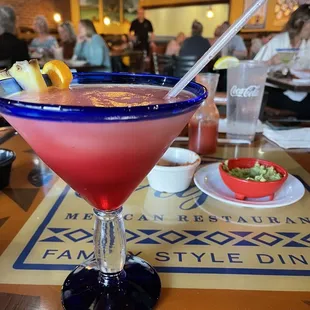 a pink cocktail in a glass with a straw and garnish garnish