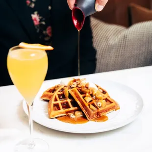 a woman pouring syrup over a plate of waffles