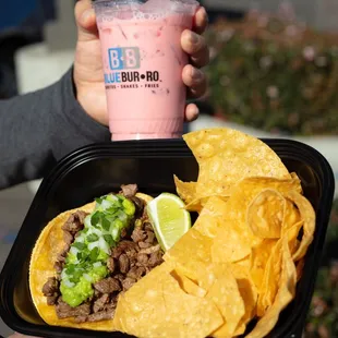 a person holding a tray of nachos and a drink