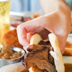 a person holding a sandwich over a plate of food