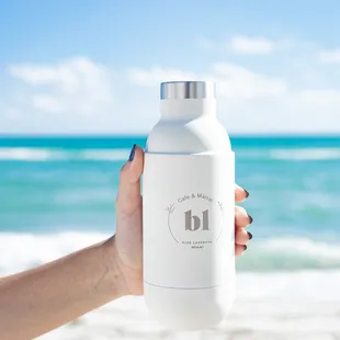 a hand holding a bottle of lavender tea on the beach