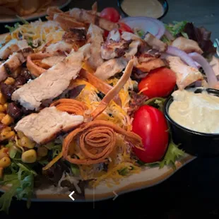 a plate of salad with chicken, lettuce, tomatoes, corn, and cheese